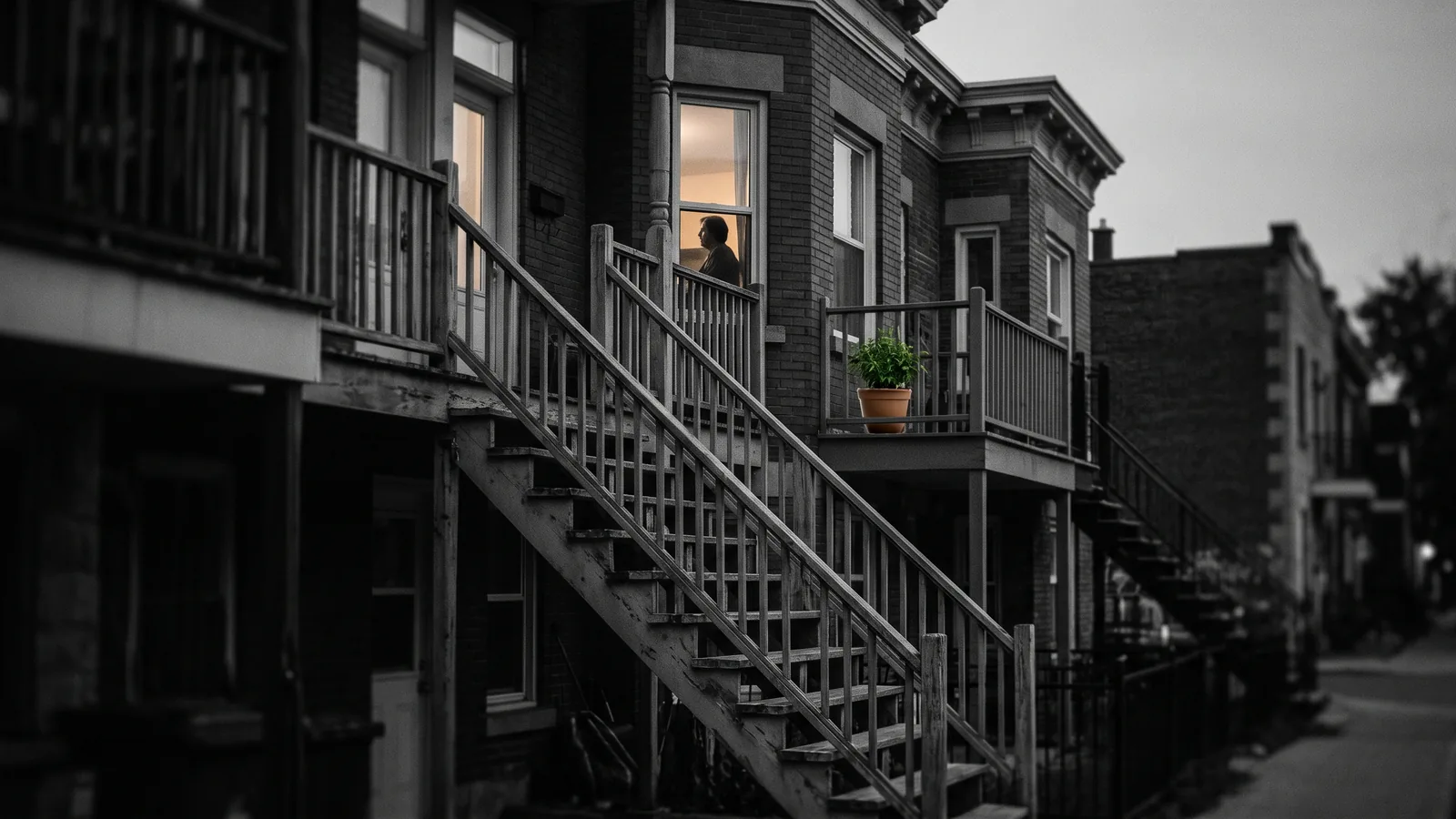 Silhouette à la fenêtre d'un triplex au crépuscule évoquant le harcèlement locataire au Québec