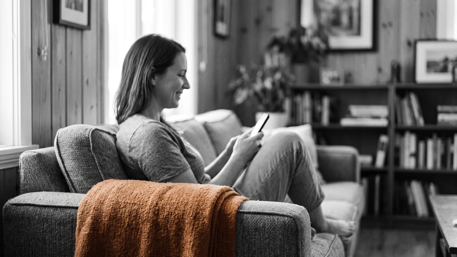 Propriétaire détendu sur un canapé lumineux, téléphone en main, plaid orange sur l'accoudoir — sérénité, services clés en main.